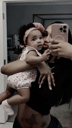 a woman holding a baby in her arms and taking a selfie with an iphone