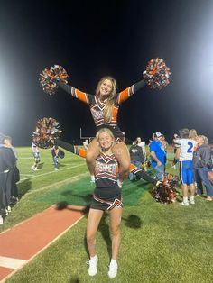 two cheerleaders on the sidelines at a football game with their hands in the air