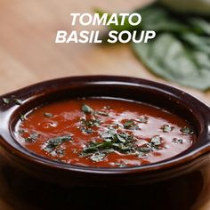 tomato basil soup in a brown bowl on a wooden table next to fresh basil leaves