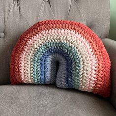 a crocheted rainbow pillow sitting on top of a gray couch