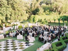 a large group of people sitting at tables on top of a grass covered field next to trees