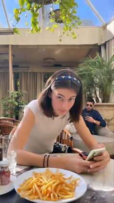 a woman sitting at a table with french fries and a cell phone in her hand