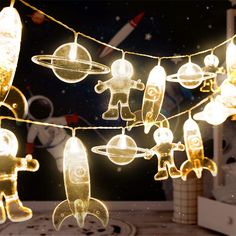 a string of lights that have space themed items on them, hanging from strings in front of a window