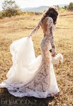 a woman in a wedding dress is walking through the grass with her back to the camera