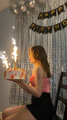 a woman sitting in front of a birthday cake with sparklers on it and the words happy birthday hanging above her