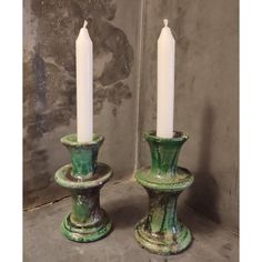 two green candle holders sitting next to each other on top of a cement floor covered ground