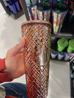 a person holding a red glass in their hand at a store with other items on the shelves