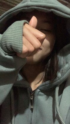 a girl in a hoodie holding her hand up to her face