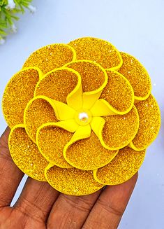 a hand holding a yellow flower brooch