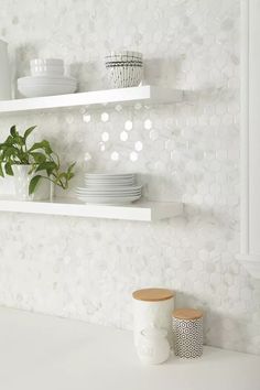 two white shelves with plates and cups on them, one has a potted plant