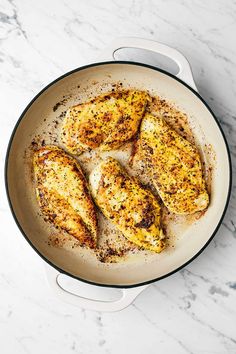 four pieces of chicken in a skillet on a marble counter top with seasoning