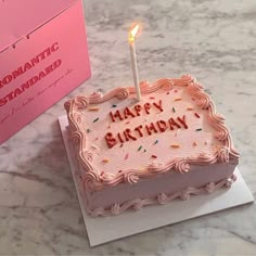 a birthday cake sitting on top of a table next to a pink box with a lit candle