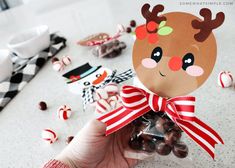 a hand holding up a bag of chocolate candies with reindeer faces on it and candy in the background