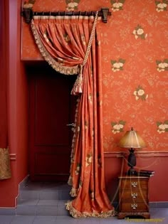 an orange room with floral wallpaper and drapes on the windowsill, along with a small chest of drawers