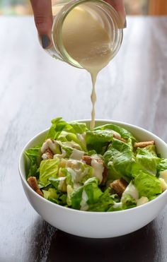 someone pouring dressing into a salad in a white bowl