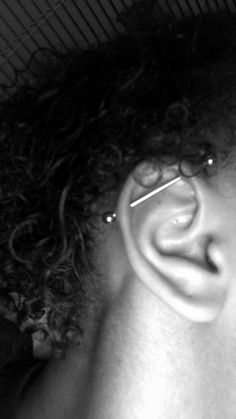 a close up of a person with curly hair wearing ear piercings on their ears