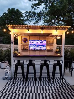 an outdoor bar set up with stools and television on the wall in the background