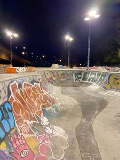 a skateboard park with graffiti on the walls and lights in the background at night