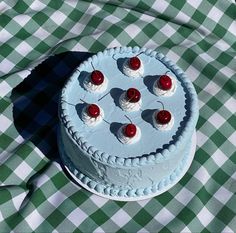 a white cake with cherries on it sitting on a green and white checkered tablecloth