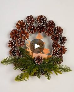 a christmas wreath made out of pine cones and evergreen branches with an ornament in the center