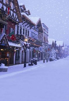 a snow covered street lined with buildings and christmas lights