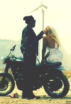 a bride and groom standing next to a motorcycle in front of wind mills with windmills behind them