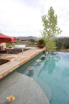 an empty swimming pool in the middle of a patio area with chairs and umbrellas