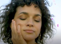 a woman with curly hair holding her hand to her face