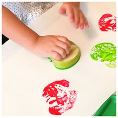 a young child is making finger prints with apple slices and apples on the counter top