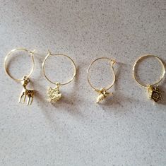 four pairs of gold filled hoop earrings with animals on them sitting on a white surface