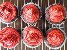 six cupcakes with red frosting sitting on a cooling rack