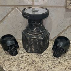 three black skulls are sitting on the counter next to a candle holder and two candles