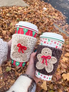 two coffee cups with crocheted designs on them are held by someone's hand