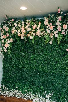 a green wall with pink flowers and greenery on the top, in front of a wooden floor