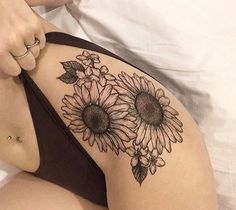 a woman laying on top of a bed with sunflowers tattooed on her thigh