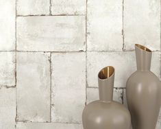 two gray vases sitting next to each other in front of a white brick wall