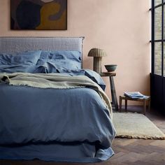 a bed with blue sheets and pillows in a bedroom next to a painting on the wall