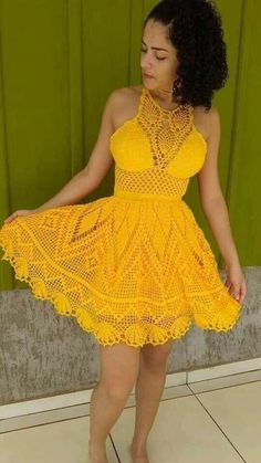 a woman wearing a yellow crochet dress standing in front of a green wall