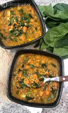 two black bowls filled with vegetable soup on top of a table next to spinach leaves