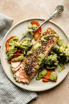 a plate with salmon, broccoli and carrots on it next to a fork