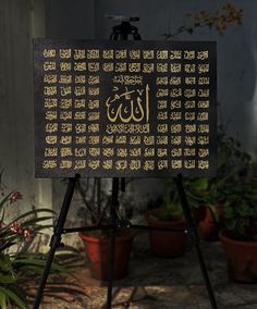 a sign with arabic writing on it sitting in front of potted plants and flowers