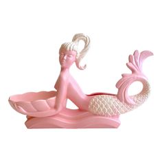 a pink and white figurine sitting on top of a boat with a mermaid tail