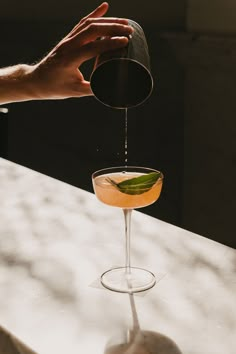 a person pours a drink into a glass on top of a table with another hand