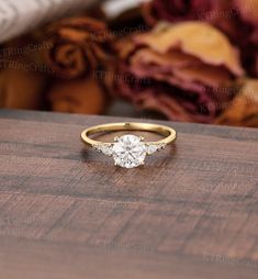 a gold ring with a single stone diamond on it sitting on top of a wooden table