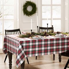 the table is set for christmas dinner with pine cones and greenery on it, along with two black chairs