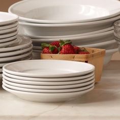 a stack of white plates and bowls with strawberries in the middle one is empty