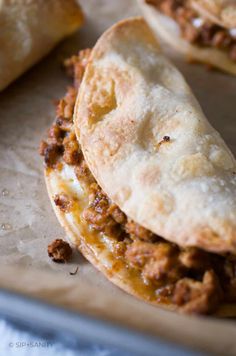 two pita breads with meat and cheese on them sitting on a baking sheet