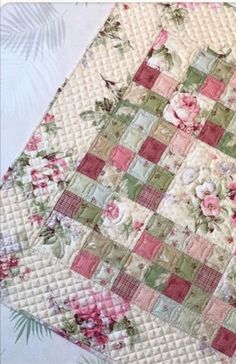 a quilted table topper with pink and green flowers on the edges, sitting on a white surface