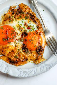 a plate with eggs and tomatoes on it next to a fork, knife and napkin