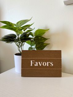 a wooden sign sitting on top of a white table next to a potted plant